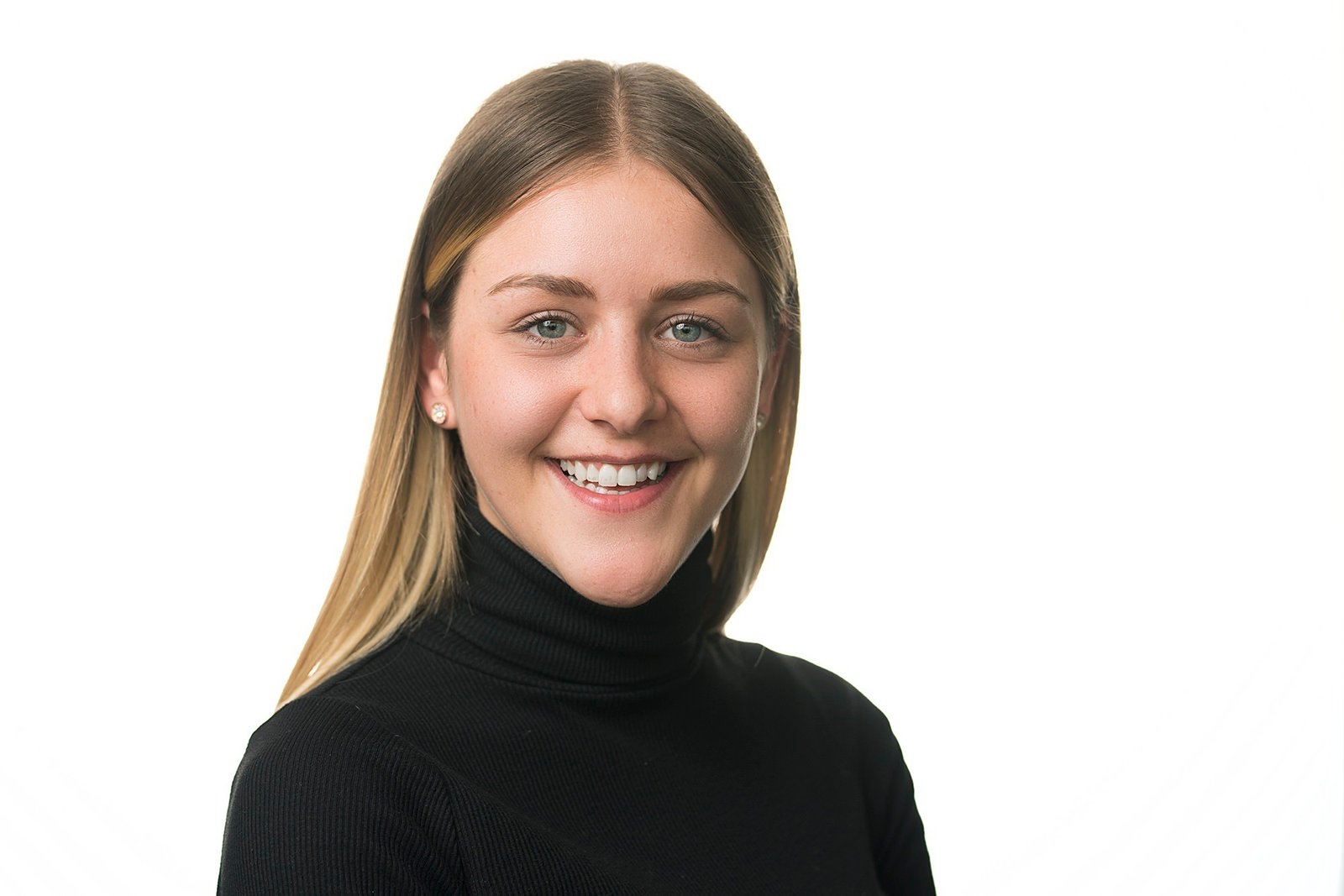 A person with long hair is smiling and wearing a black turtleneck sweater. They are posed against a plain white background. James Gifford-Mead Photography - Event Photographer London