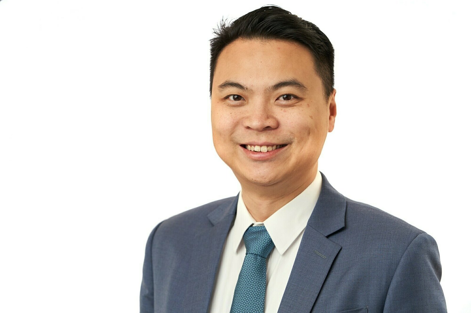 A man in a blue suit and tie smiles at the camera. The background is plain white, creating a professional and clean look
