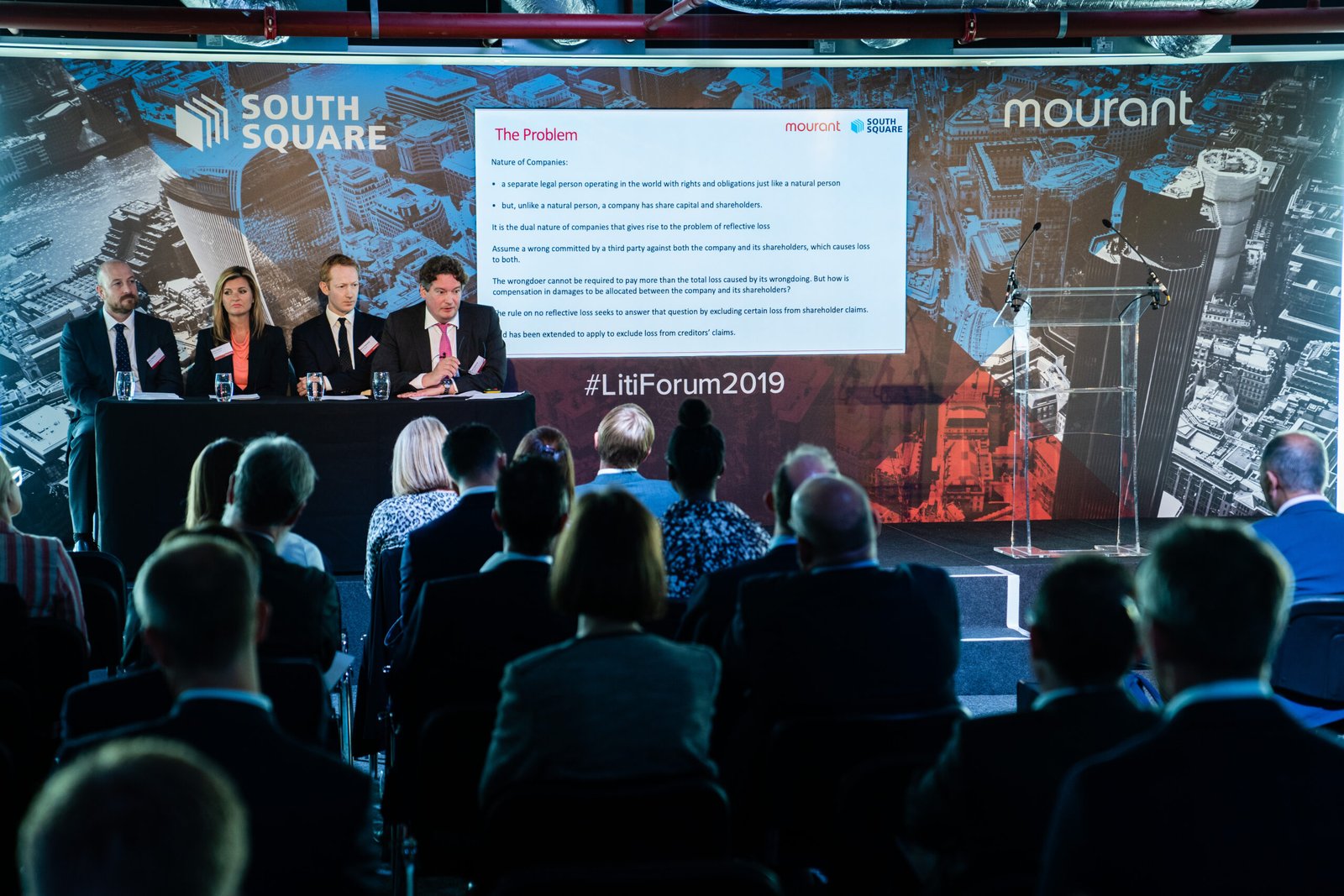 A panel of four people sits at a table on a stage, facing an audience. A presentation slide titled "The Problem" is projected on a screen next to them. The event is branded with "South Square" and "Mourant" logos. Attendees are seated in rows. James Gifford-Mead Photography - Event Photographer London