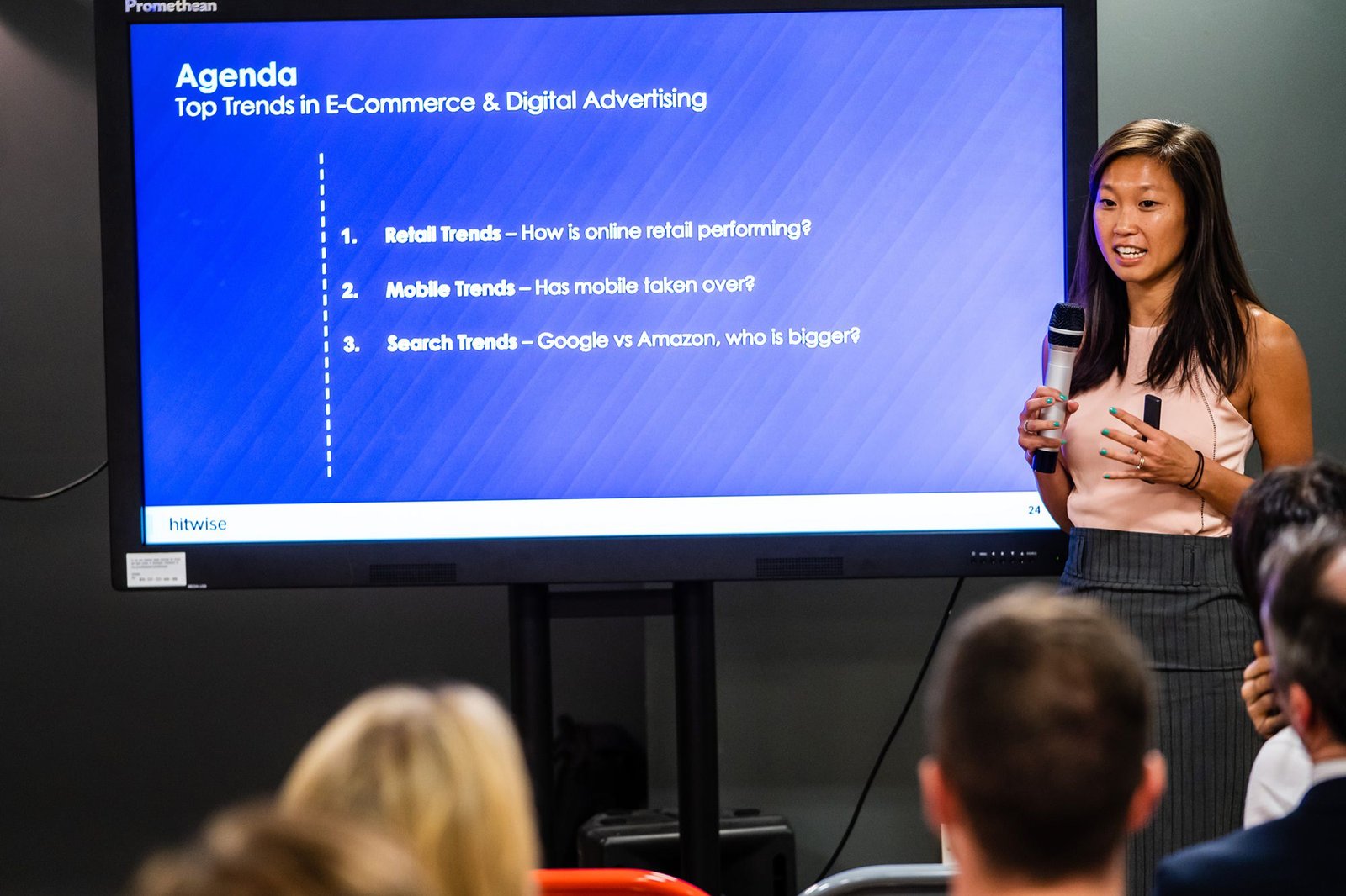 A person stands in front of a screen giving a presentation on "Top Trends in E-Commerce & Digital Advertising," with points on retail, mobile, and search trends. The audience is seated in the foreground. James Gifford-Mead Photography - Event Photographer London