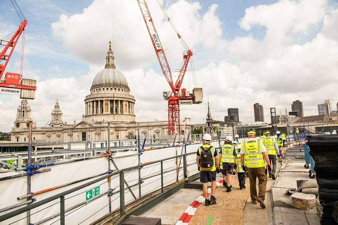 Construction workers, wearing safety vests and helmets, navigate the site with cranes and equipment. Captured by a corporate photographer in London, St. Paul's Cathedral and the skyline paint a stunning backdrop under the partly cloudy sky. James Gifford-Mead Photography - Event Photographer London