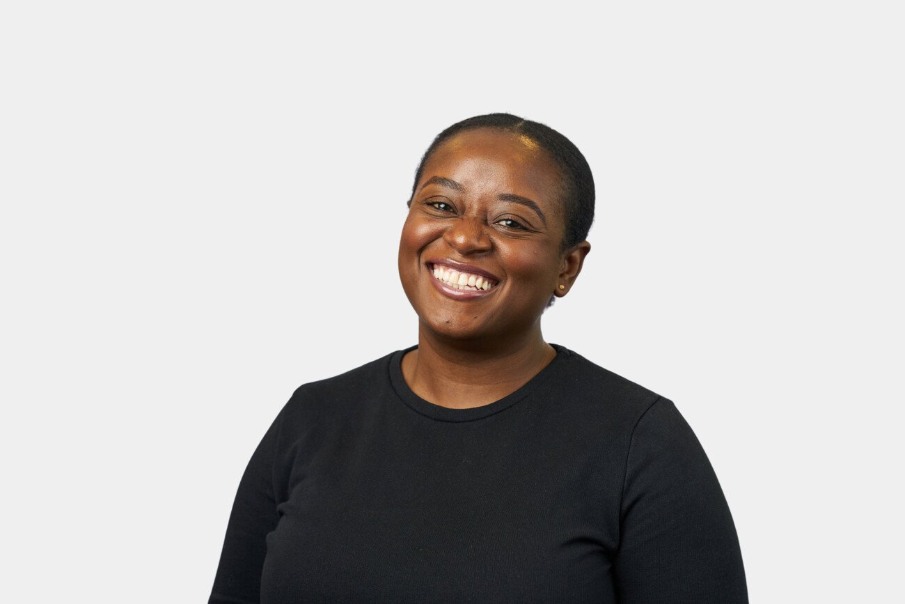 A smiling person with short hair wearing a black top poses against a plain white background, showcasing the clean, professional touch of a corporate headshot photographer. James Gifford-Mead Photography - Event Photographer London