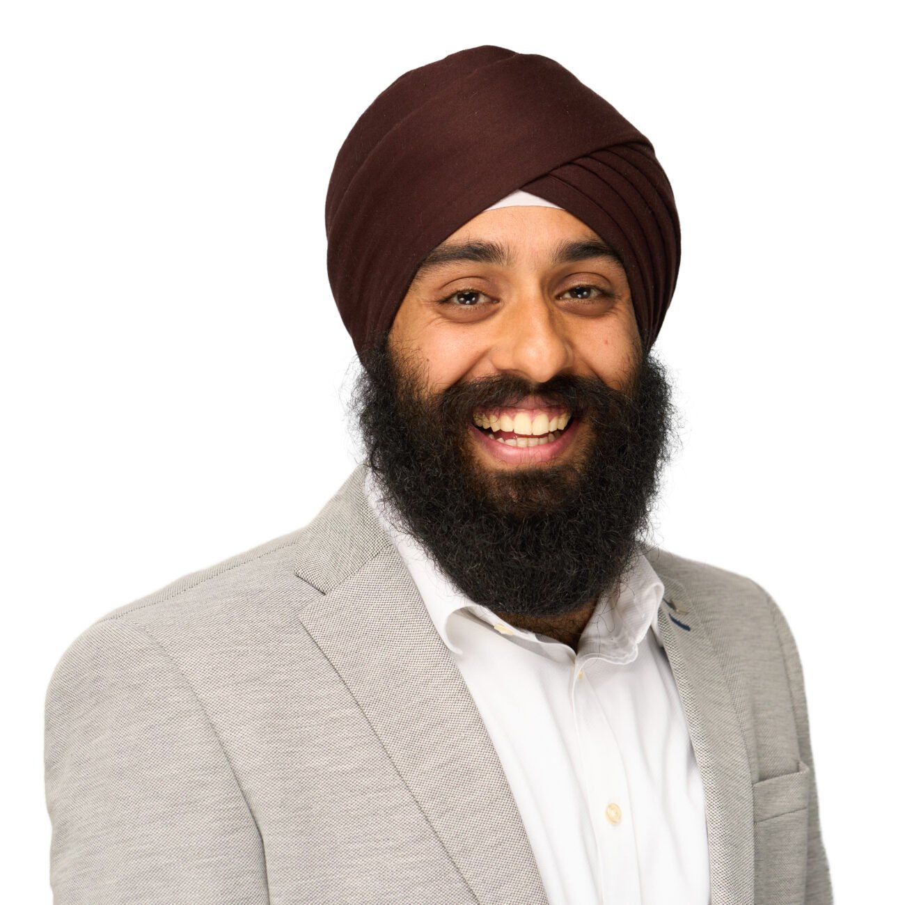 A person wearing a brown turban and a light gray blazer smiles warmly against a plain white background, capturing the professionalism and approachable nature that any corporate headshot photographer strives to achieve. James Gifford-Mead Photography - Event Photographer London