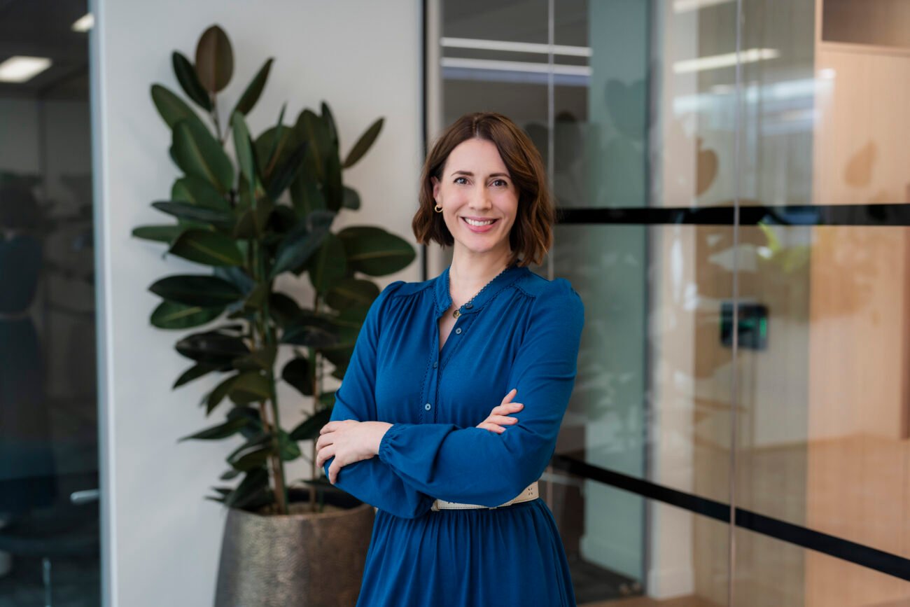 Smiling woman in office with plant background.