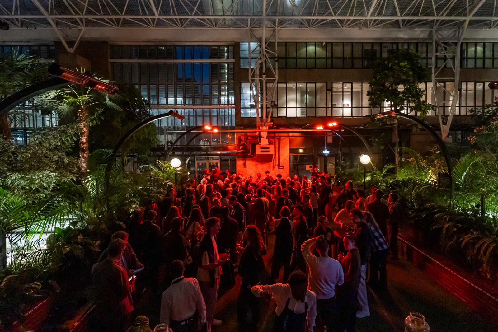 Crowd enjoying night event in greenhouse garden.