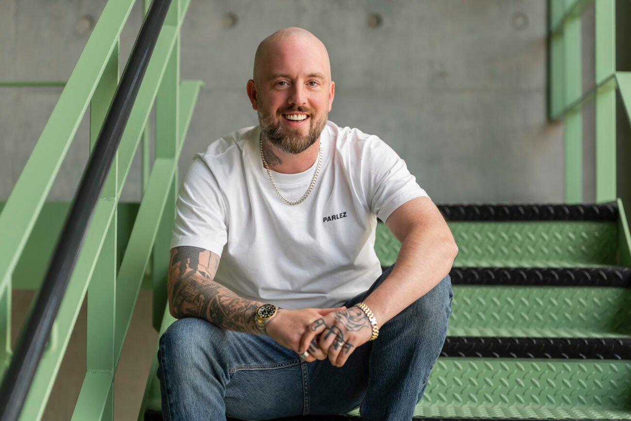 Smiling man with tattoos sitting on green stairs.