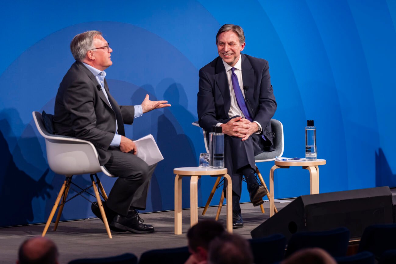 Two men in discussion on stage with blue background.