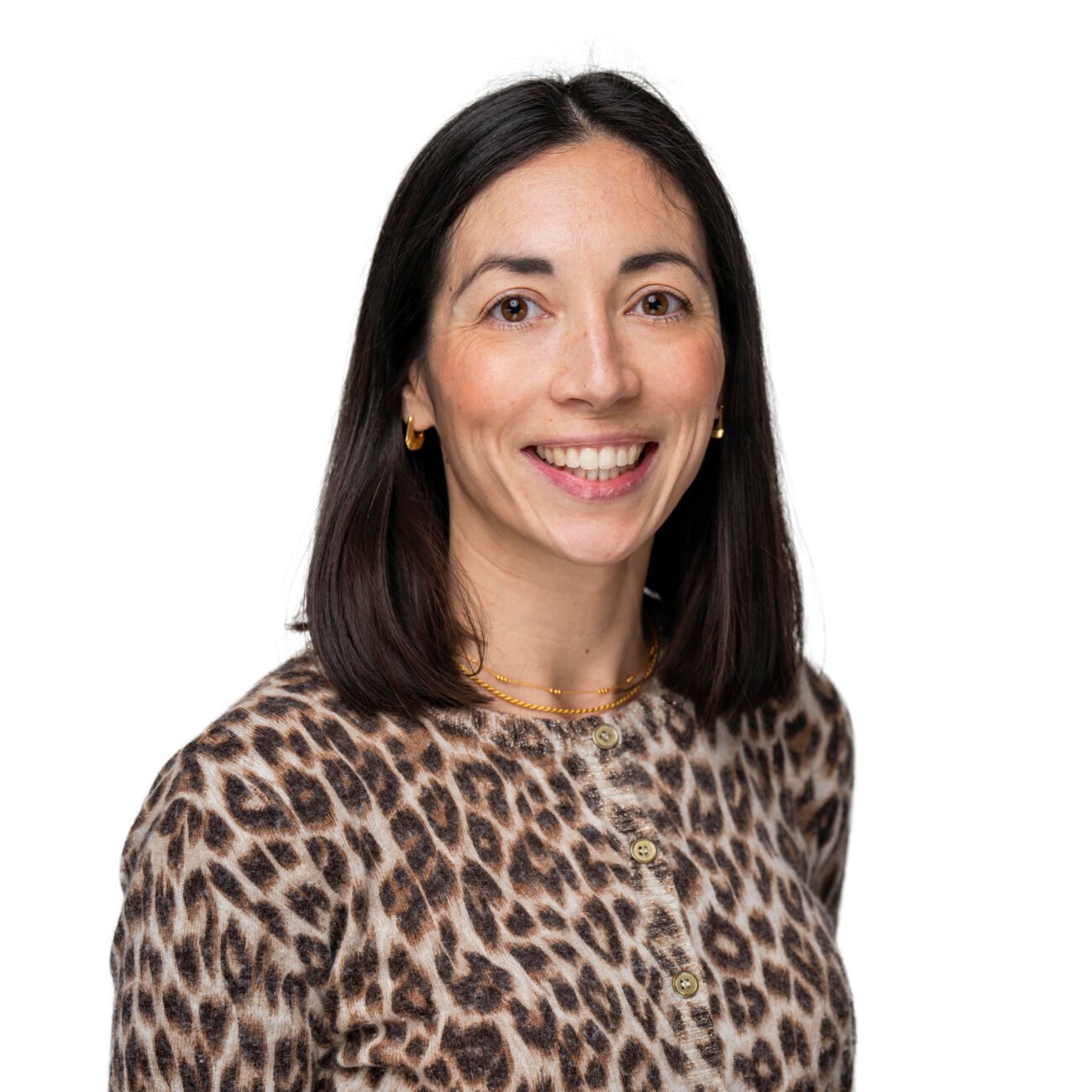Woman with straight dark hair, wearing a leopard print shirt and gold jewellery, smiling at the camera against a plain white background—captured in a polished style by a Corporate Headshot Photographer.
