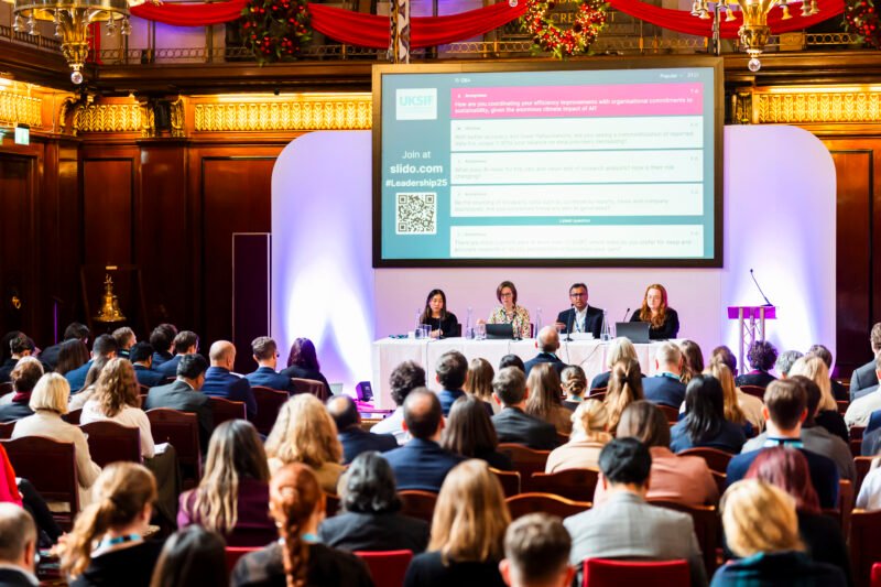 Conference panel discussion with audience in hall.