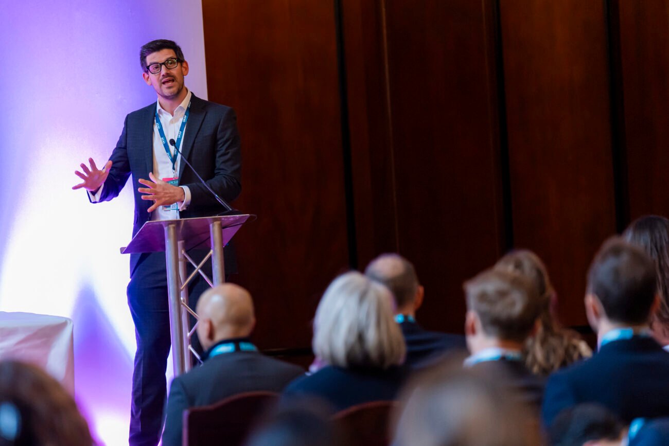 Man presenting at business conference to seated audience.