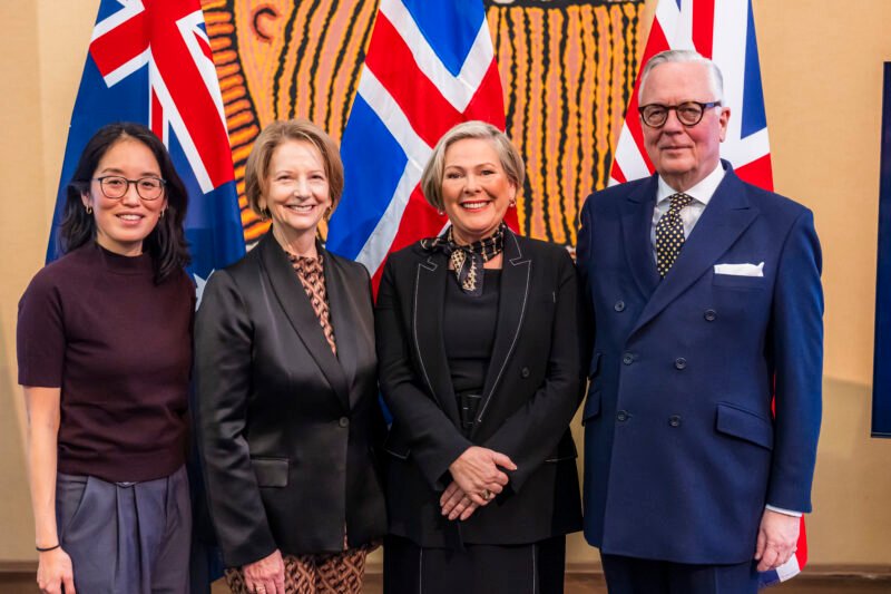 Four people smiling, standing in front of flags.