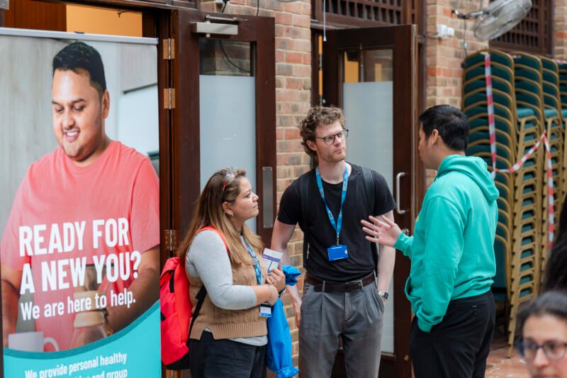 Three people discussing by health promotion poster.