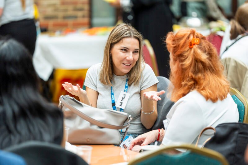 Two women talking at a conference table.