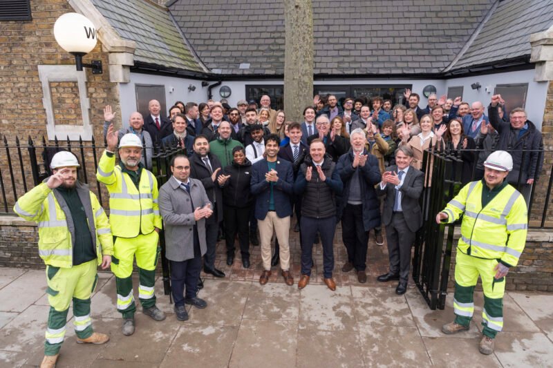 Group celebrating outside building, construction workers included.