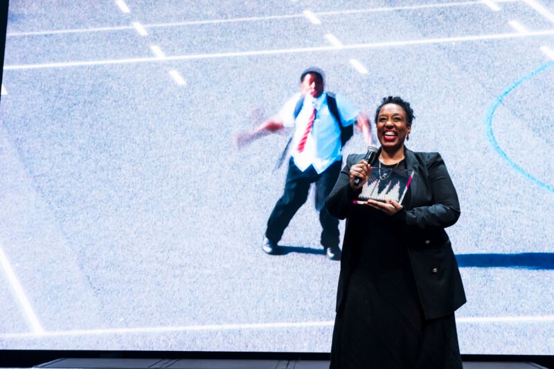 Smiling woman presenting an award on stage.
