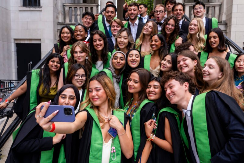 Graduates in gowns taking a group selfie.