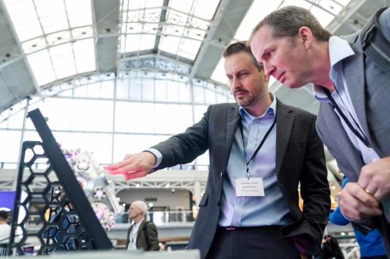 Businessmen discussing technology at a conference booth.